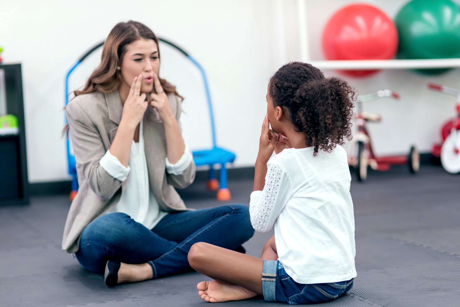 Adult female therapist guiding young girl in speech therapy